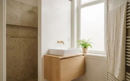 Minimalistische Amsterdamse badkamer met lichte eiken wastafelmeubel, wit keramisch wasbak en ingepot plantje op de vensterbank in natuurlijk daglicht.