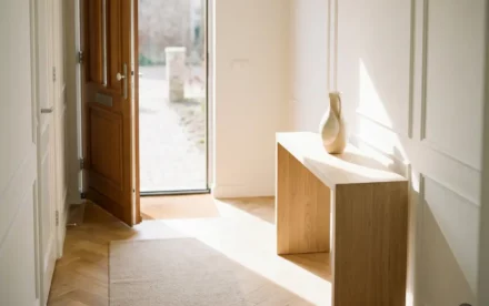 Zonnige Nederlandse hal met licht eiken visgraatparket, minimalistische sidetable met keramische vaas en halfopen voordeur.