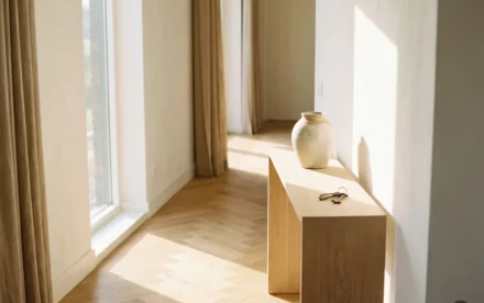 Zonnige Nederlandse hal met licht eiken visgraatparket, witte muren, keramieken vaas en huissleutels op een sidetable bij een hoog raam.