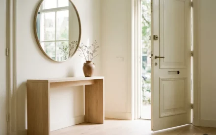 Lichte Nederlandse hal met eiken vloer, keramische vaas op sidetable en licht openstaande voordeur in warm natuurlijk licht.