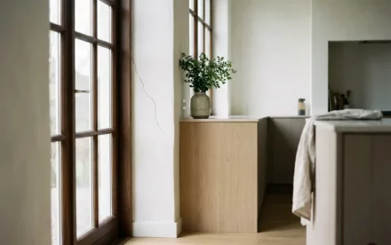 Haarscheur in witte pleisterwand naast vensterkozijn in minimalistische Nederlandse keuken met licht eiken vloer en natuurlijk daglicht.
